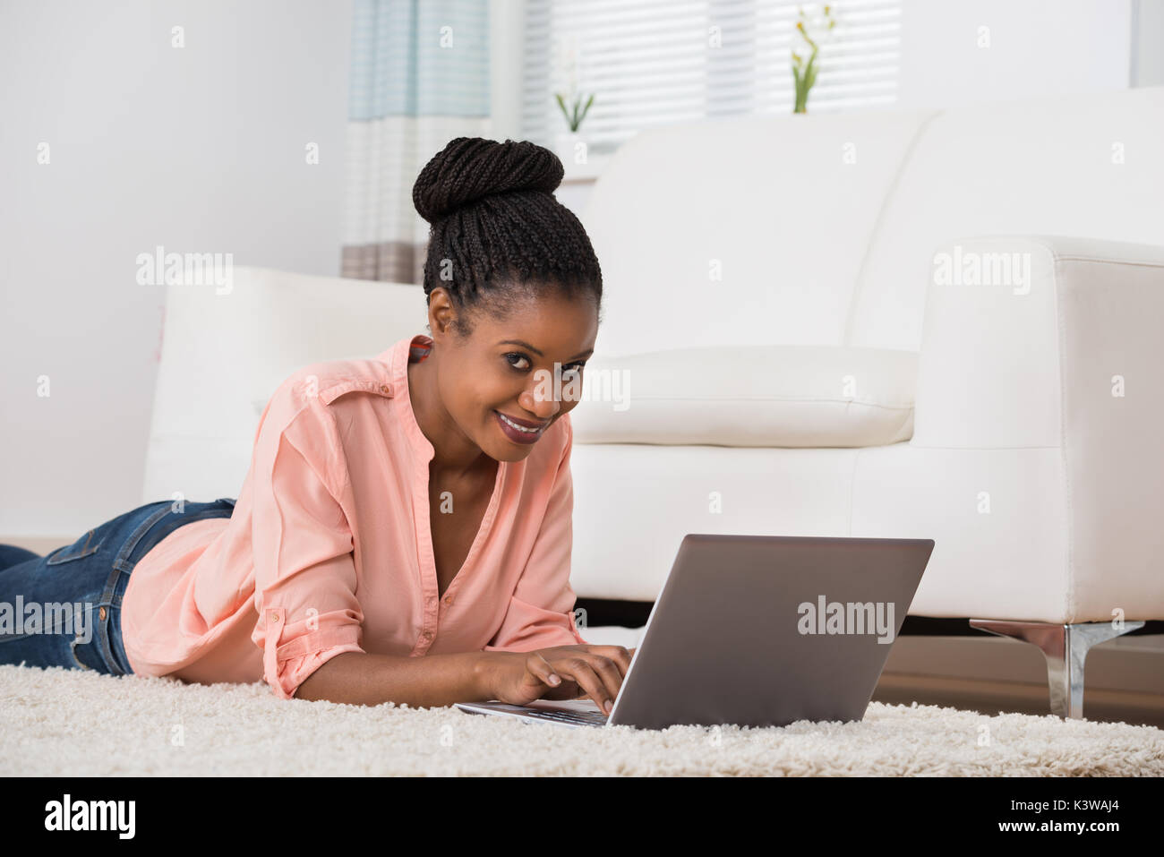 Portrait Of A Smiling Young African Woman Lying On Carpet Using Laptop ...