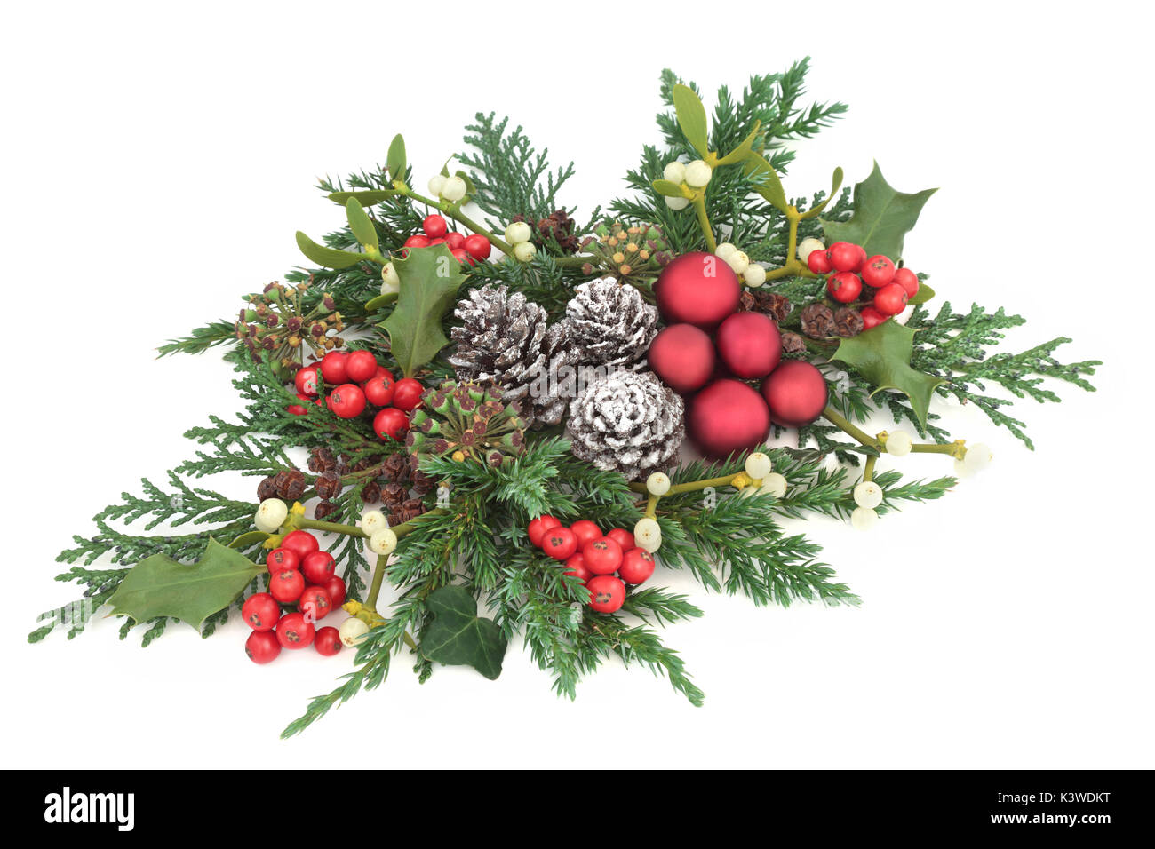 Christmas fauna with red bauble decorations, holly, ivy, mistletoe, cedar and juniper leaf sprigs and pine cones on white background. Stock Photo