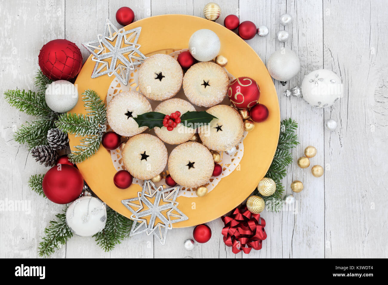 Christmas mince pies on a gold plate with holly, fir, red and white ...