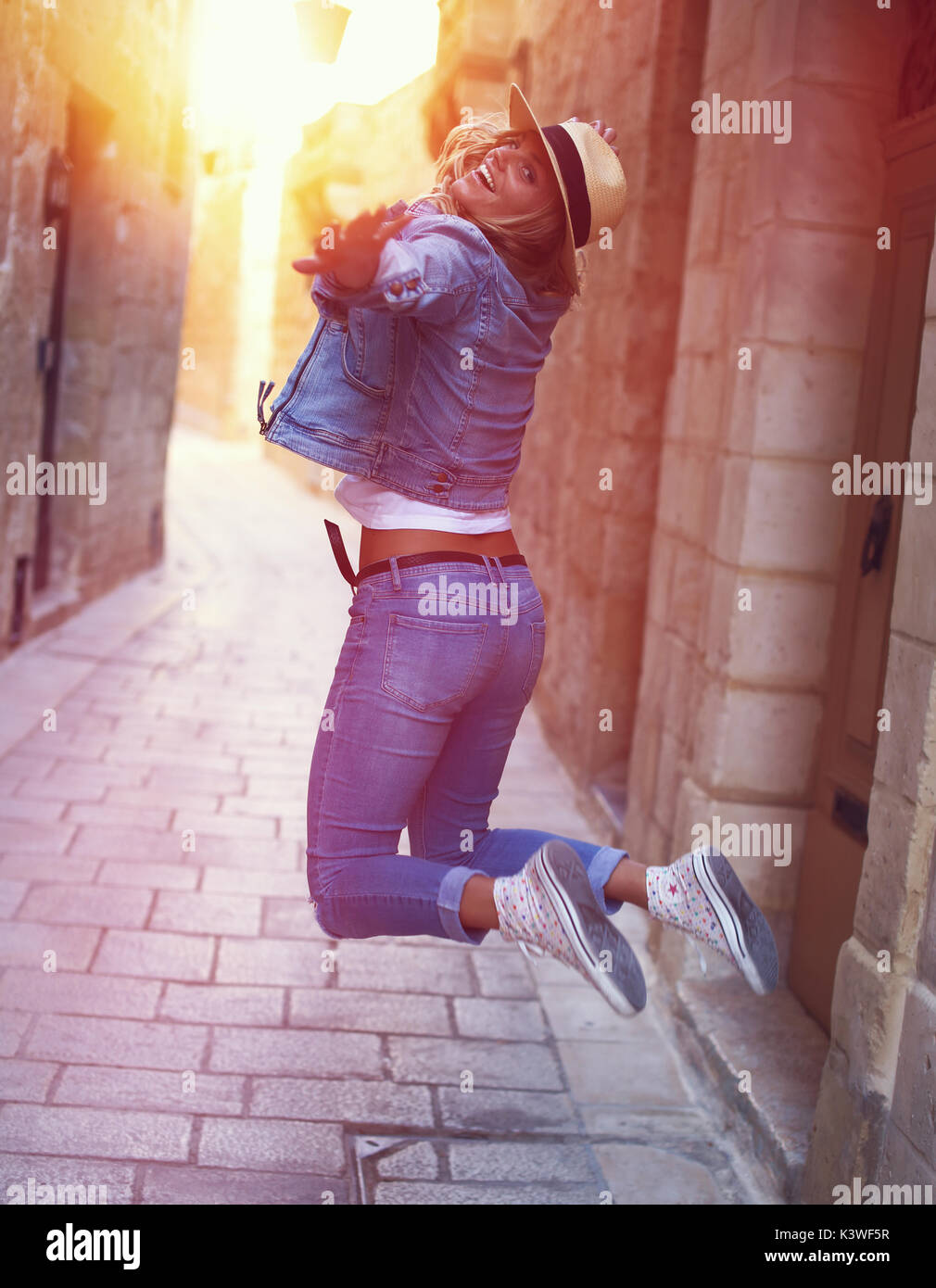 Happy carefree woman jumping on mediterranean street in sunset Stock Photo