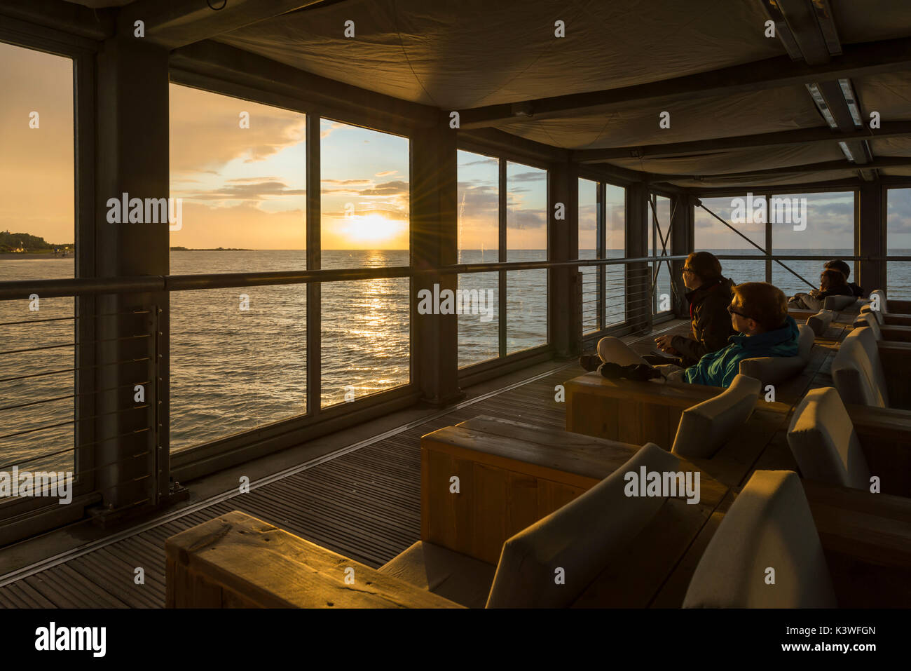 Menschen beobachten durch die Panoramafenster der Seebrücke von Heiligenhafen den Sonnenuntergang über dem Meer Stock Photo