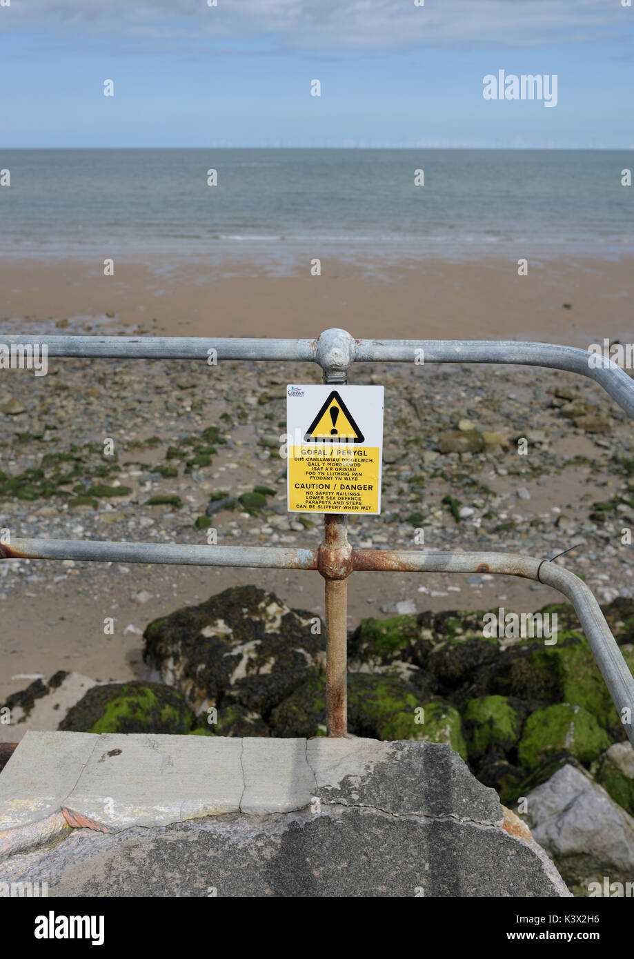 Corroded handrail risk warning sign and warning sign overlooking beach in north wales uk Stock Photo