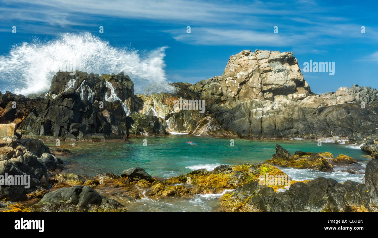 Spectacular wave splashes against the rocks shielding the natural pool (Conchi), a popular tourist attraction, in Aruba. Stock Photo