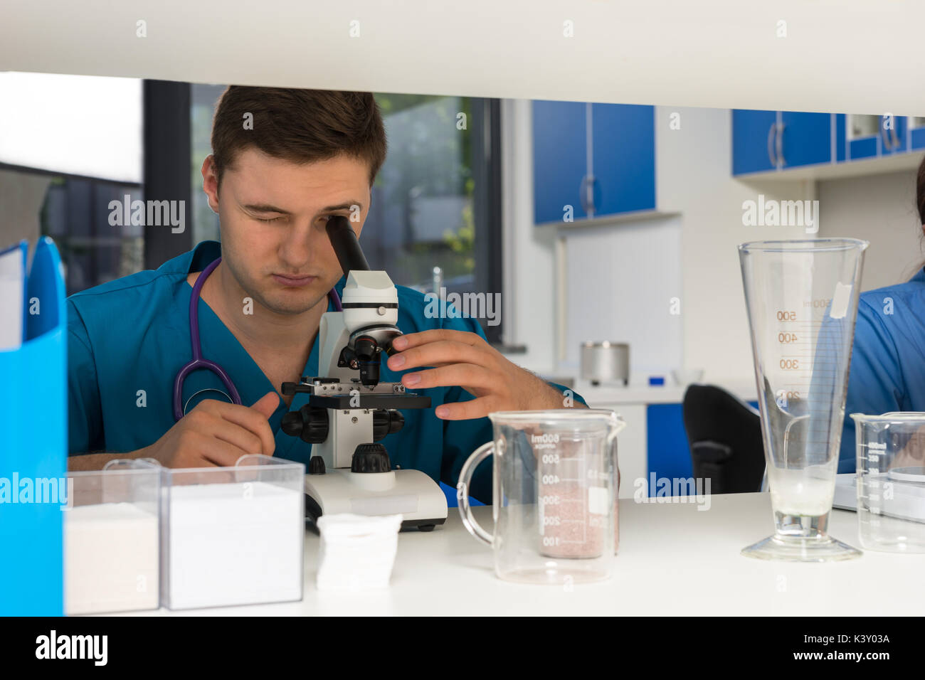 Young male scientist in uniform is looking through a microscope and making some research in a laboratory. Healthcare and biotechnology concept Stock Photo