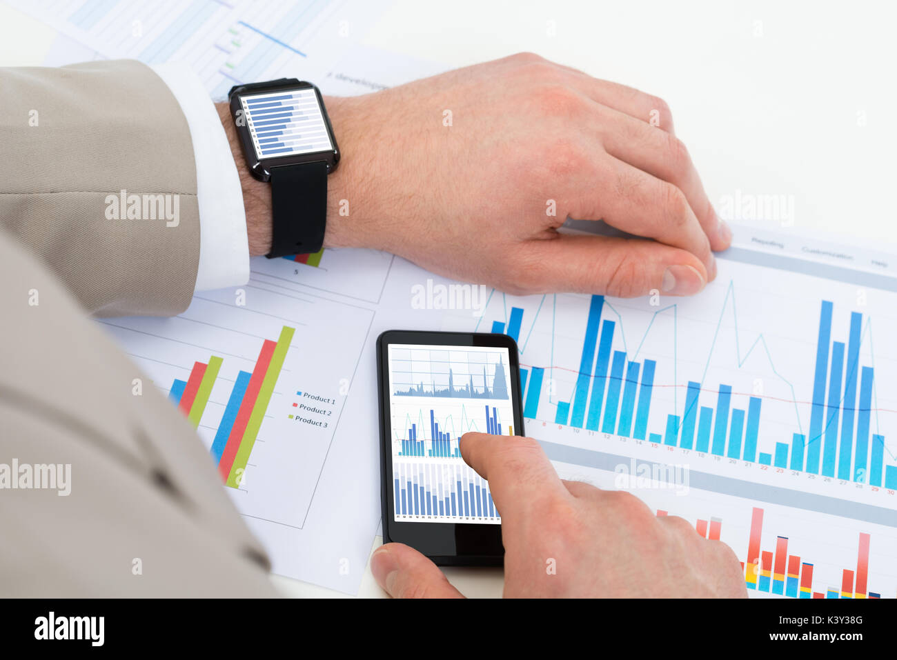 Close-up Of Businessman Analyzing Graph With Mobile Phone And Smartwatch Stock Photo