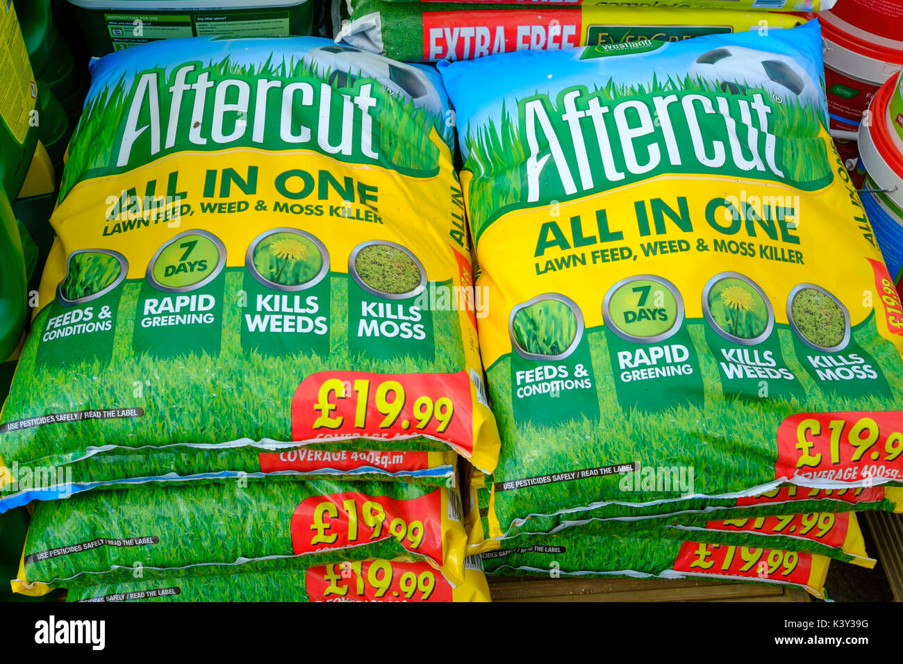 A stack of bags of Aftercut lawn feed weed and moss killer in a garden