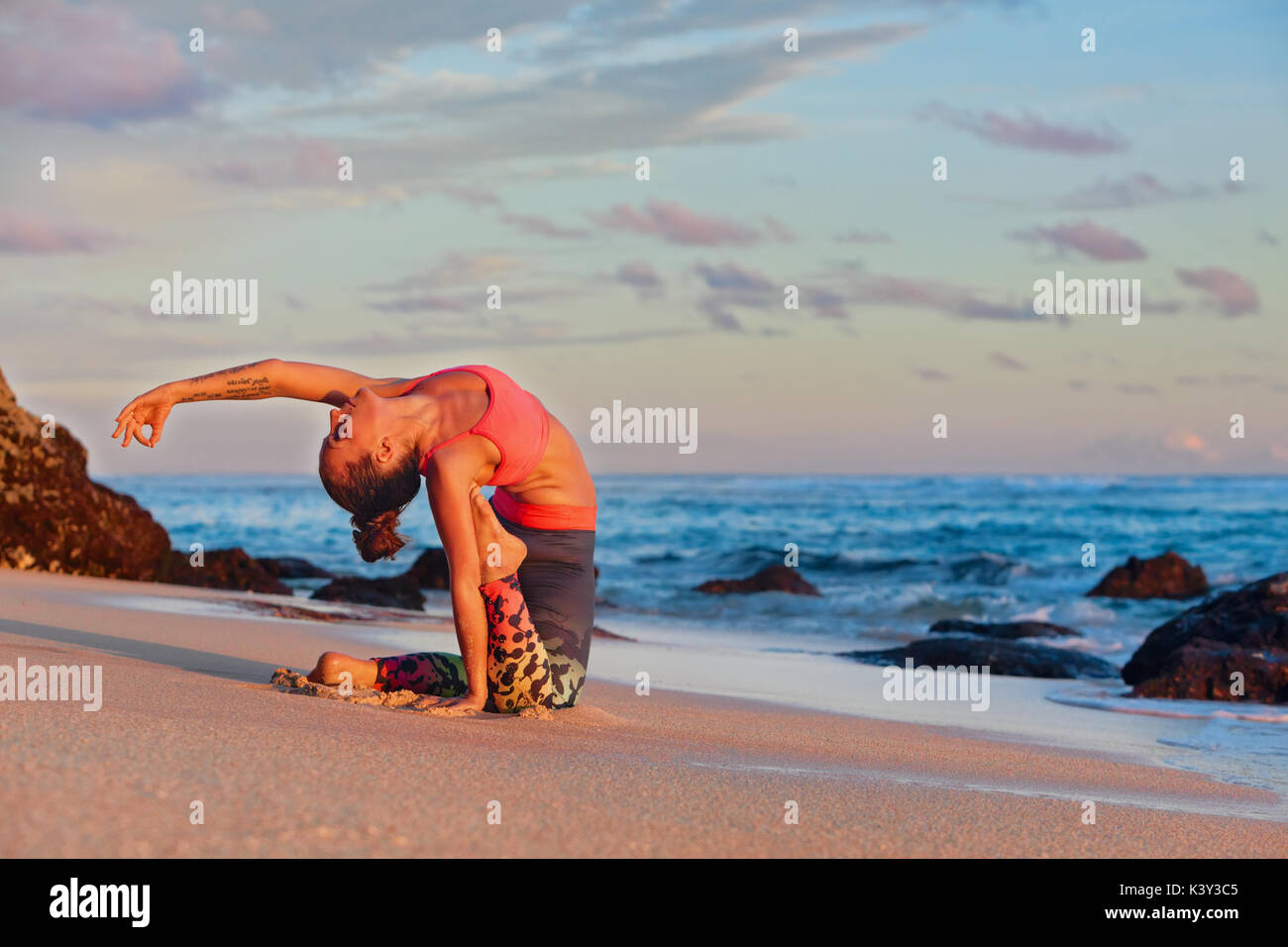 Meditation on sunset sky background. Young active woman sit in yoga pose on sand beach, stretching to keep fit and health. Healthy lifestyle, fitness Stock Photo