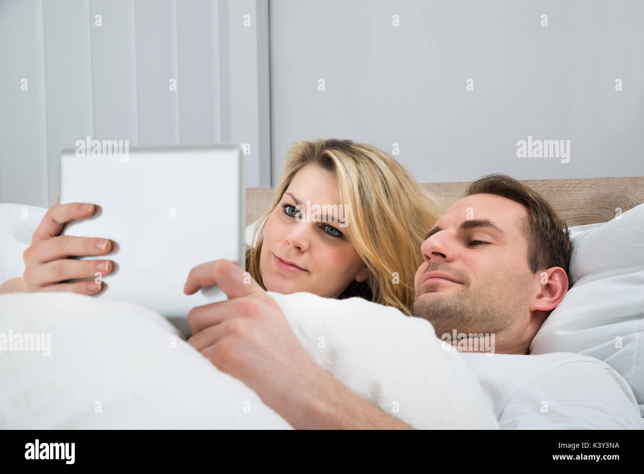 Happy Couple Using Digital Tablet In Bed At Home Stock Photo