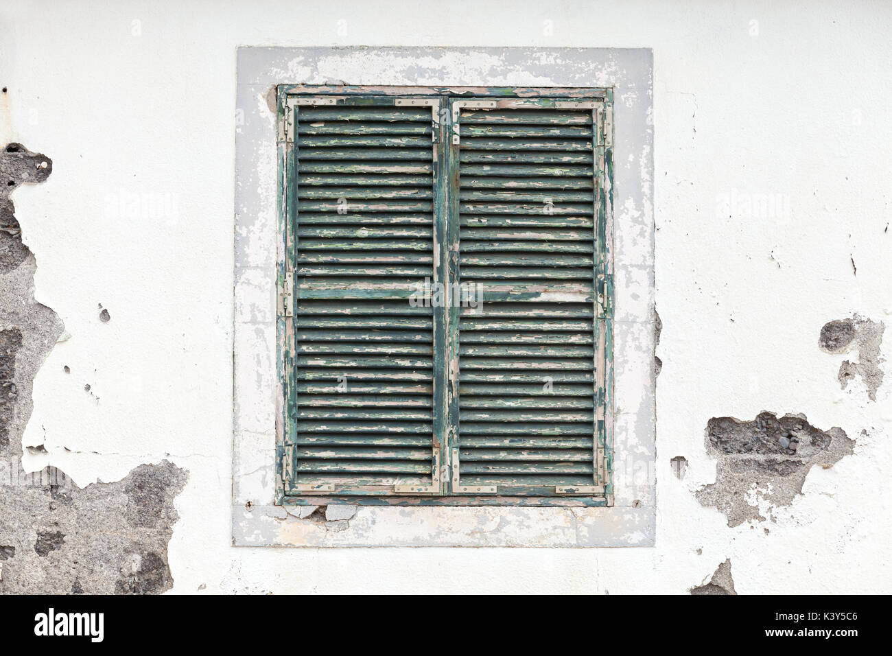 Old window with closed jalousie in white weathered wall, background texture Stock Photo