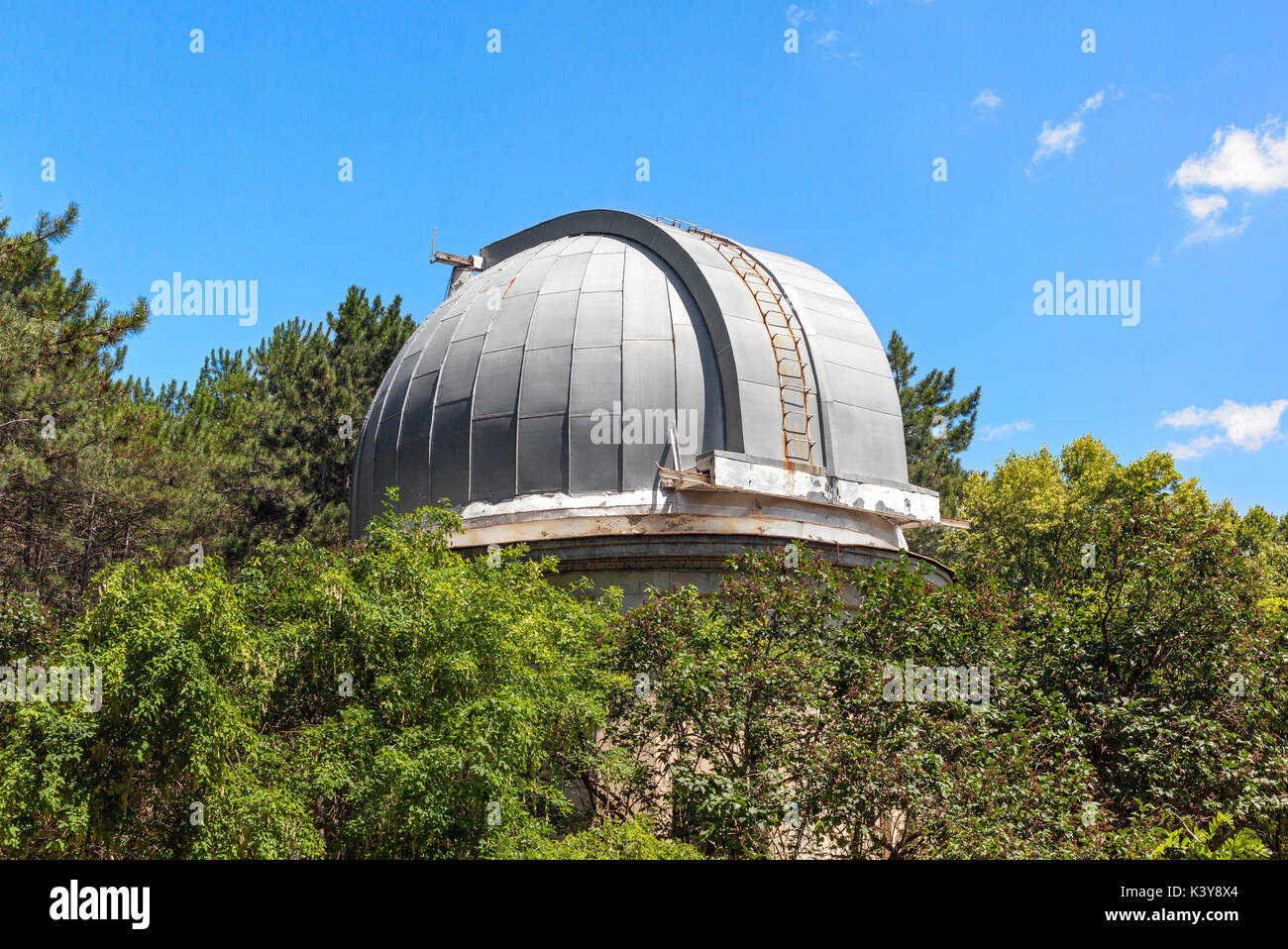 Closed dome of the old telescope in the observatory is among the crowns of trees. Stock Photo