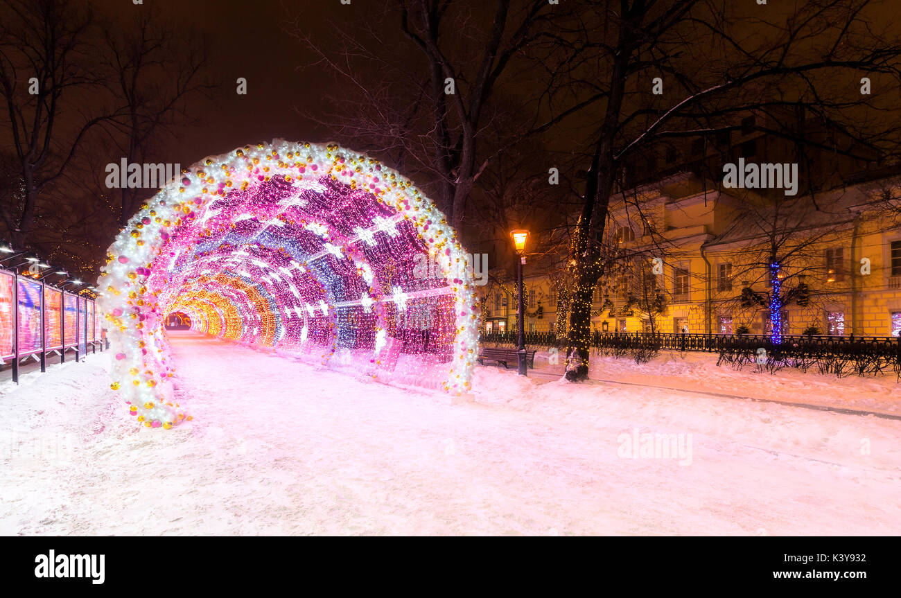 Entrance to the glowing decorative tunnel decorated with Christmas-tree toys and Christmas and New Year's attributes. City park at night in the center Stock Photo