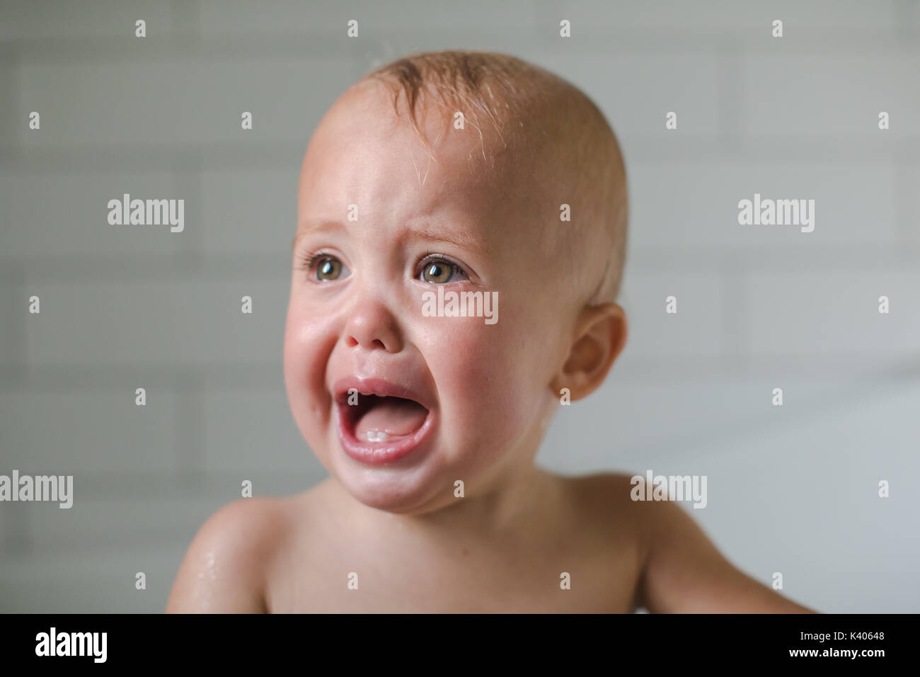 One-year-old baby cries close-up in the bathroom on a white background Stock Photo