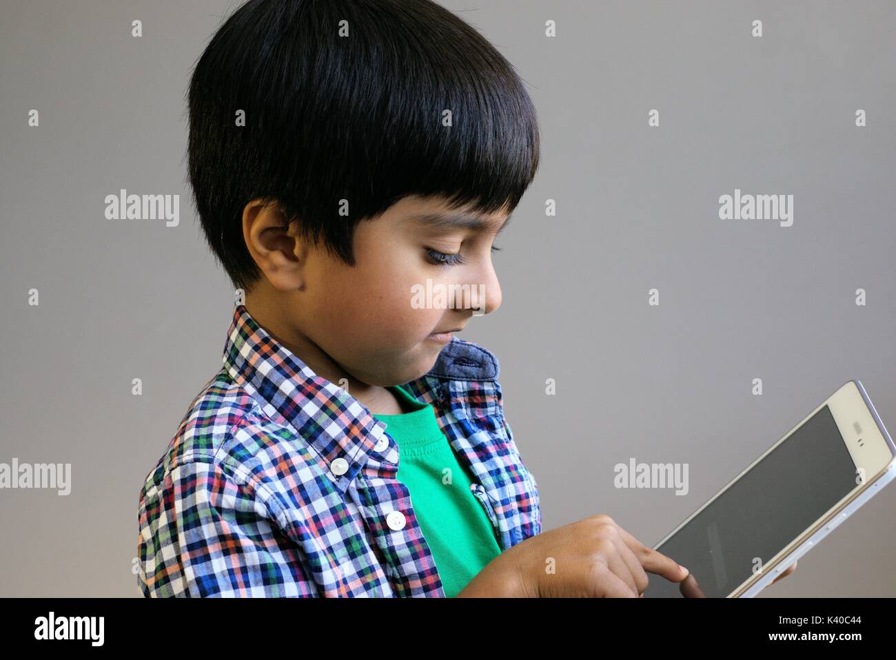Kid using technology shot in natural light. Kid wearing headphones looking at tablet computer. Child with headphones using tablet. Stock Photo