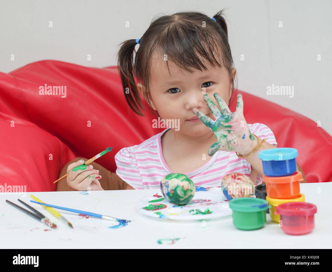 Little Girl Painting with paintbrush and colorful paints children development concept Stock Photo