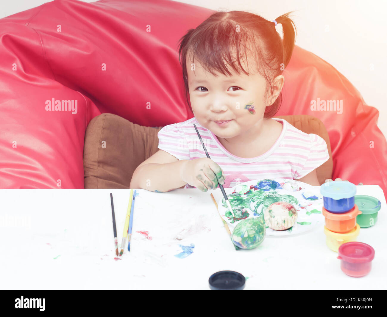 Little Girl Painting with paintbrush and colorful paints children development concept Stock Photo