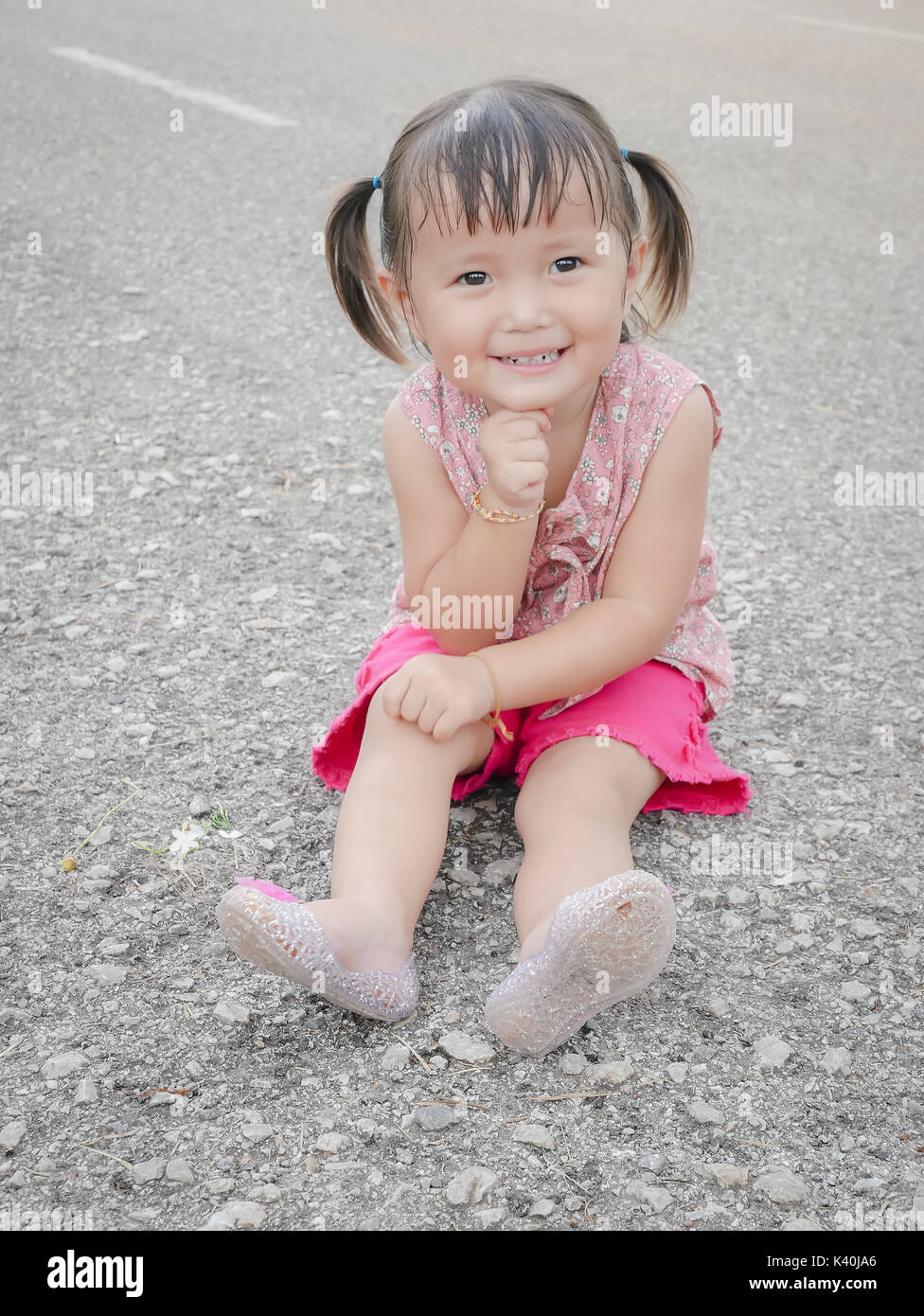 Little Asian Girl Sitting And Smiling On The Floor Stock Photo