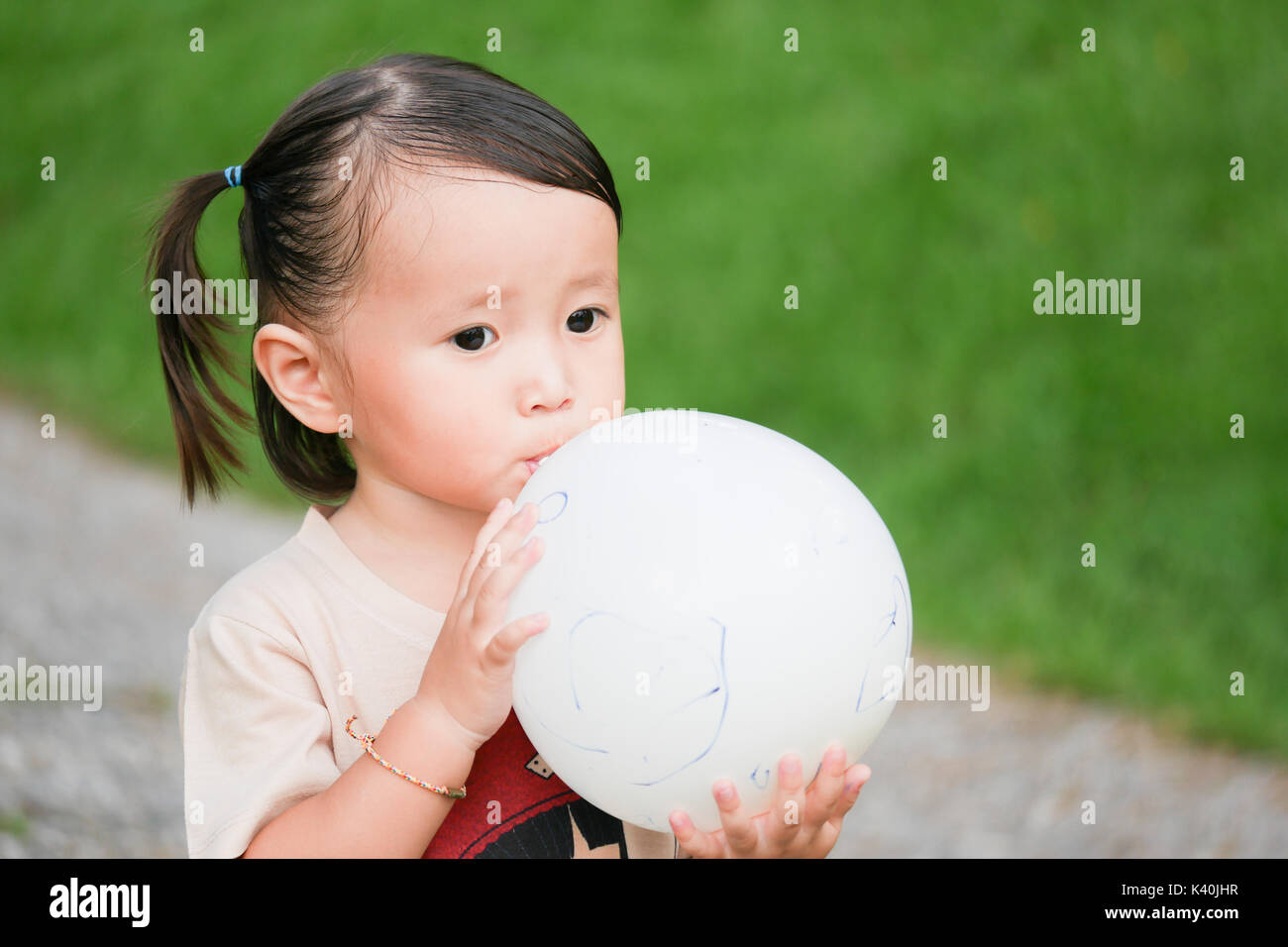 Blowing Up Balloon:Close up portrait of little girl blowing up a balloon in the green garden Stock Photo