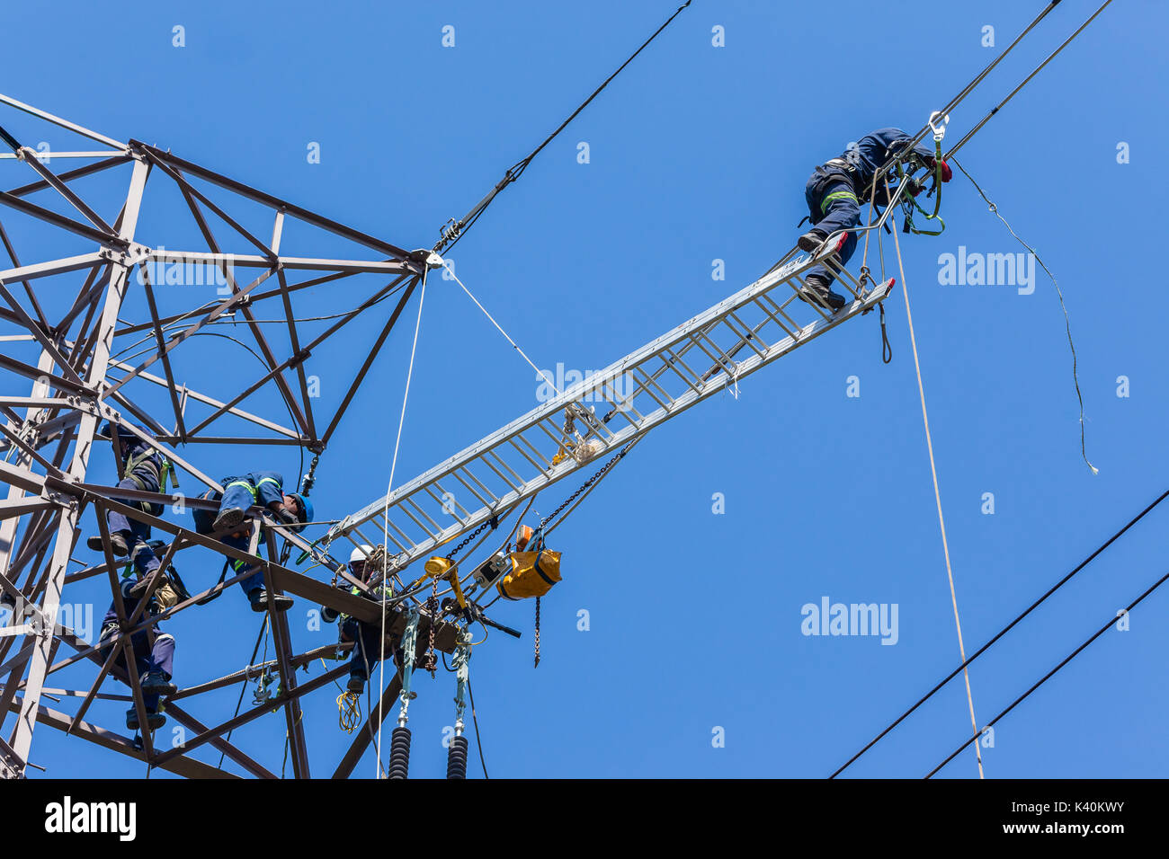 Electricians workers hanging high on power line cables doing maintenance repairs to electrical cables. Stock Photo