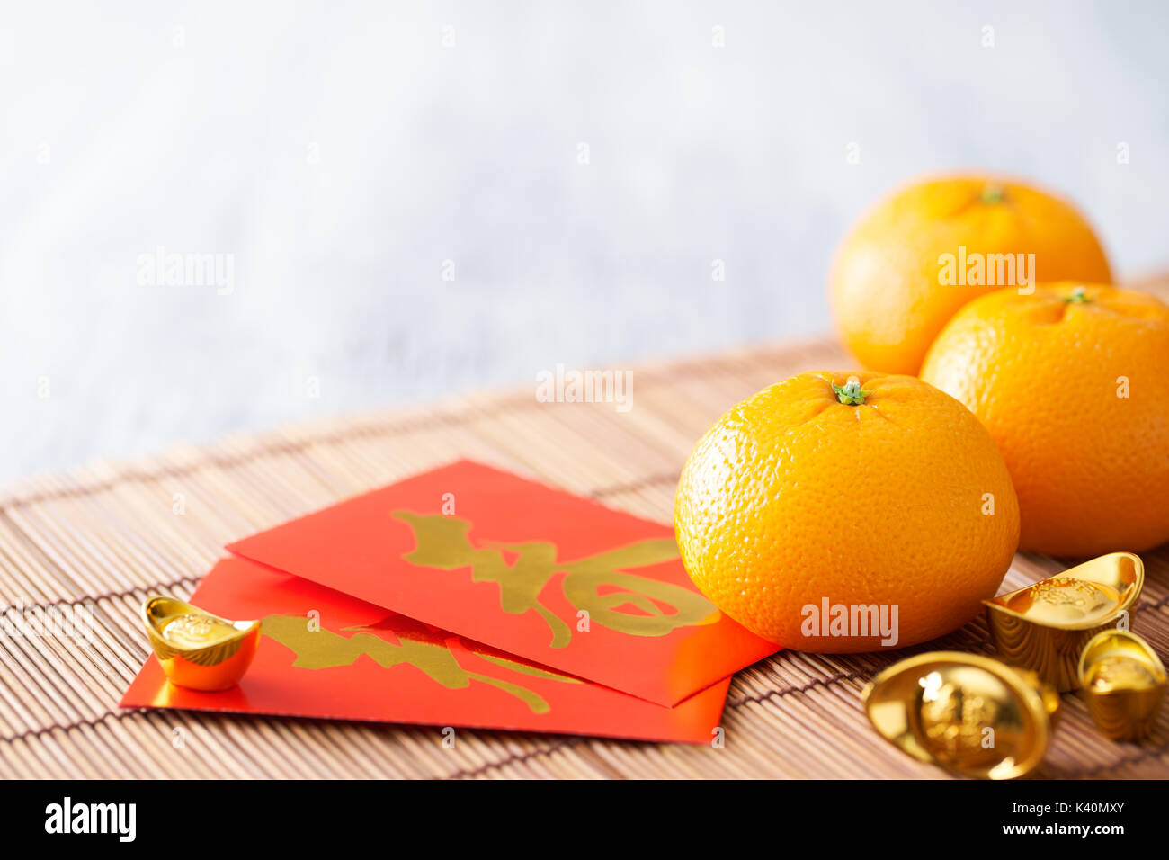 Chinese New Year - Mandarin orange, gold sycee (Foreign text means wealth) and red packet (Foreign text means spring season) on white painted wood tab Stock Photo