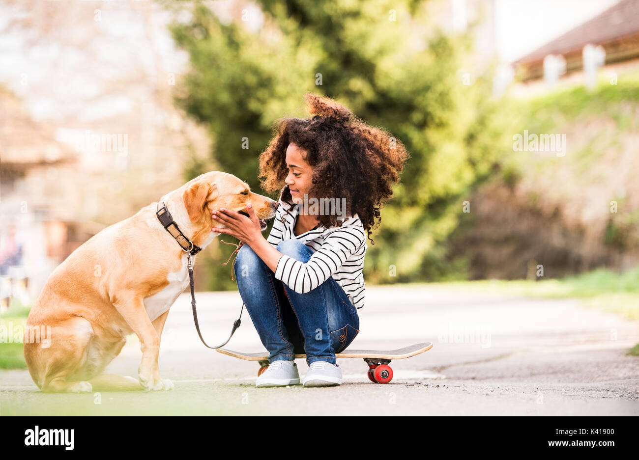 African american girl outdoors on skateboard with her dog. Stock Photo