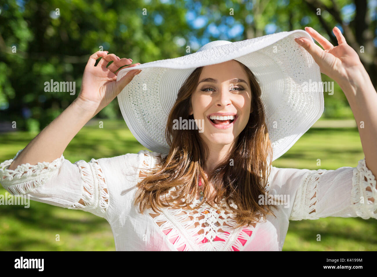 Front portrait of happy young woman standing in park holding hat Stock Photo