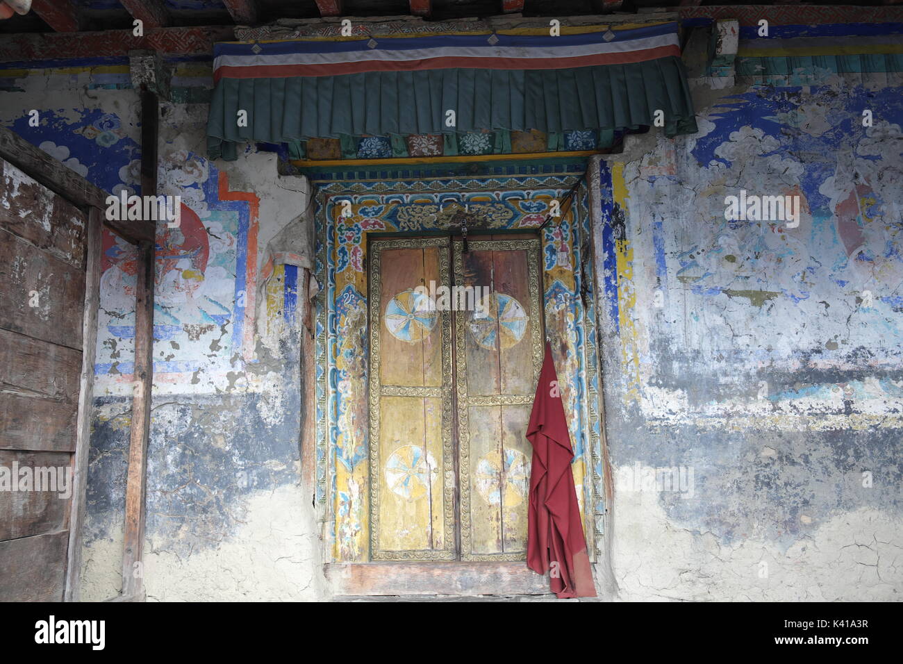 Monks Red Robe Hanging on Door with Tibetan Art Painting at Mu Gompa Monastery, Nepal on Tibetan Border in the Tsum Valley Remote Region Stock Photo
