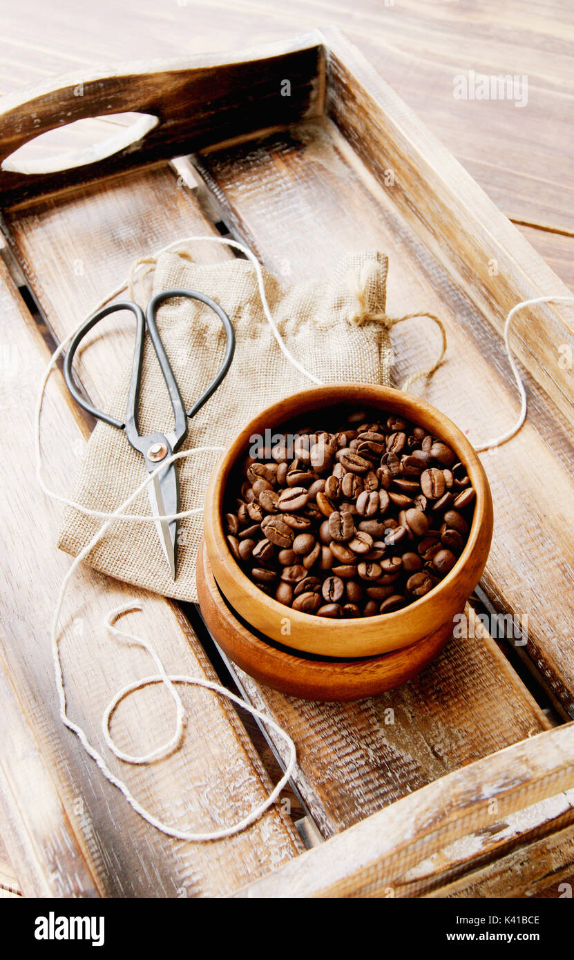 coffee beans in a wooden bowl with a canvas bag, scissors and thread on a wooden table, selective focus Stock Photo