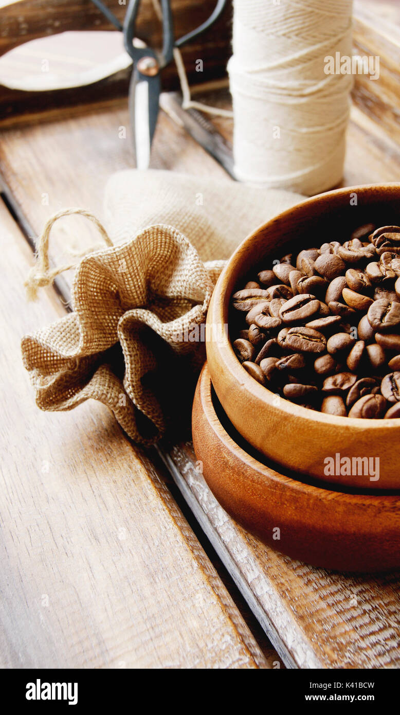 coffee beans in a wooden bowl with a canvas bag, scissors and thread on a wooden table, selective focus Stock Photo