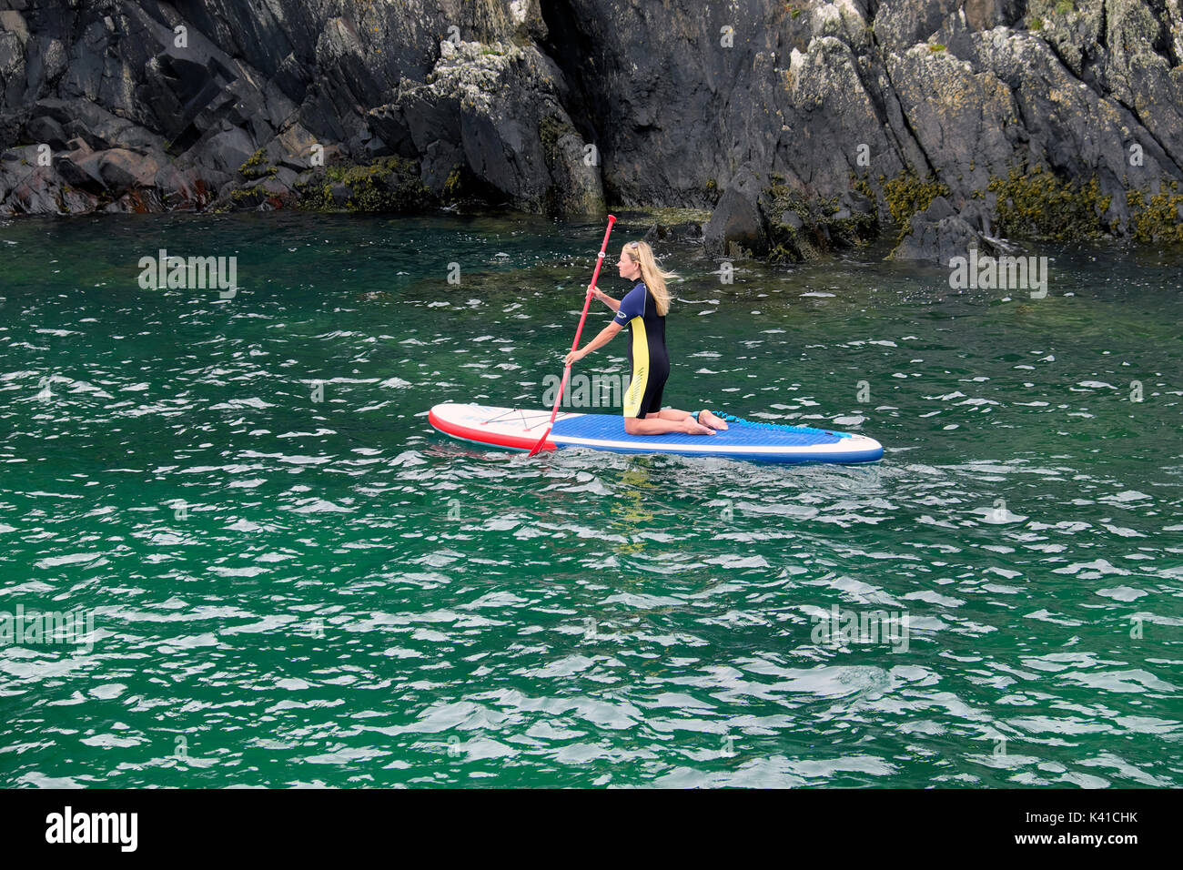 A woman in a wetsuit paddleboarding in Porthclais Harbour towards St
