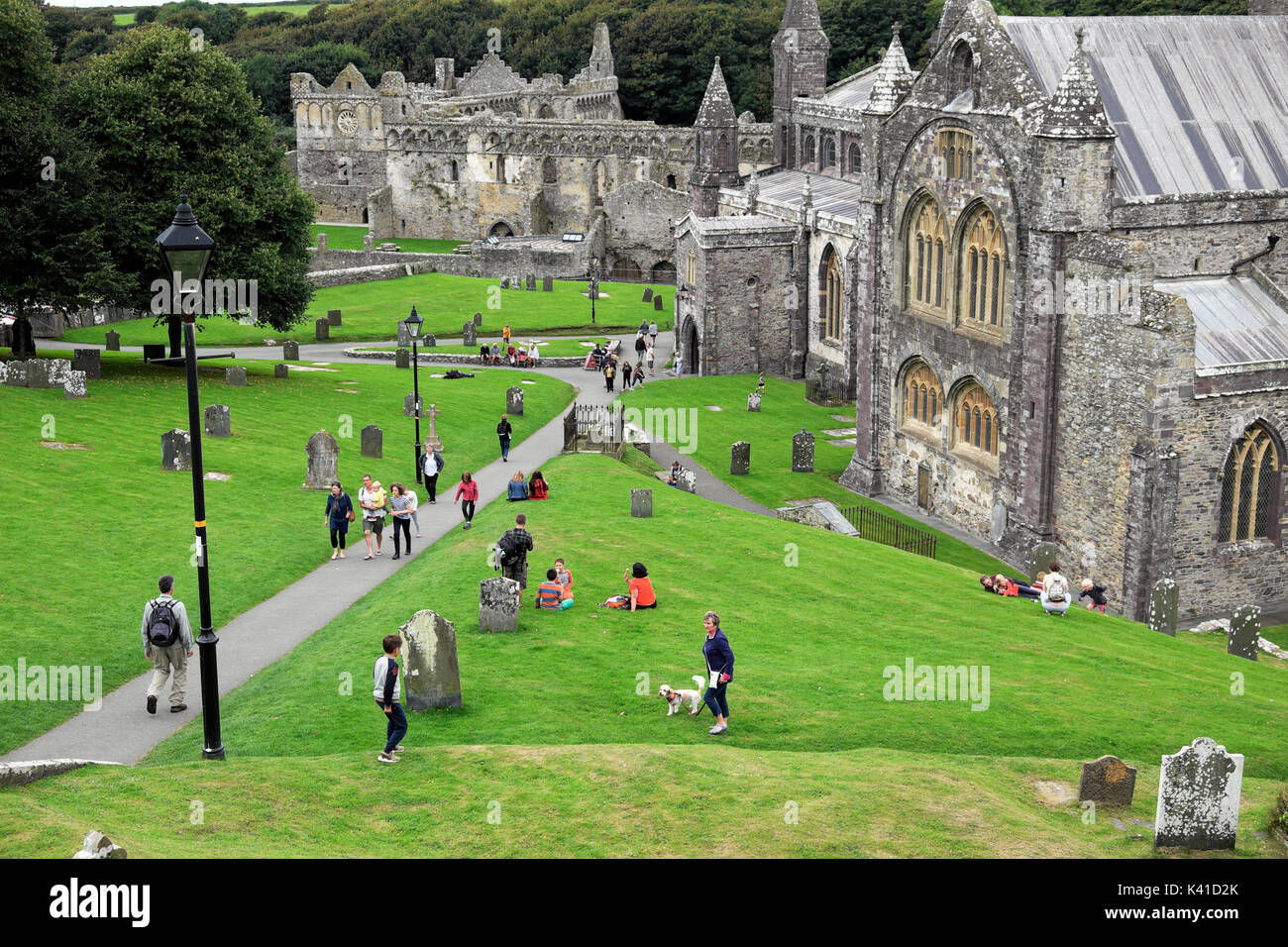 People visitors walking on the lawn in summer outside St. David's Cathedral, Pembrokeshire, Wales UK  KATHY DEWITT Stock Photo