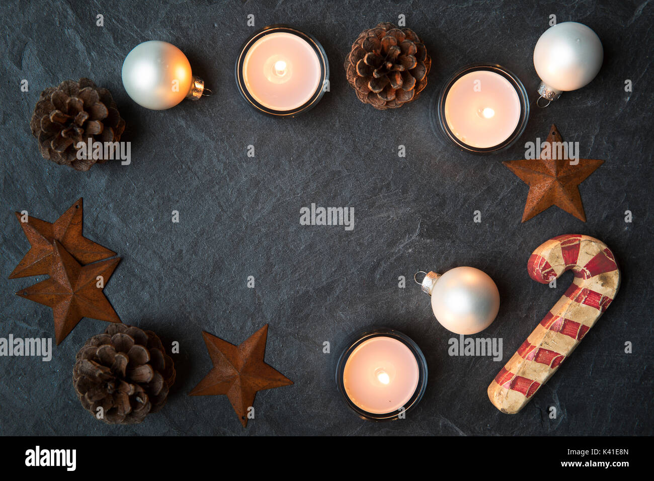 Rustic Christmas decorations and tea lights on dark stone surface with copy space in the center.  Viewed from directly above Stock Photo