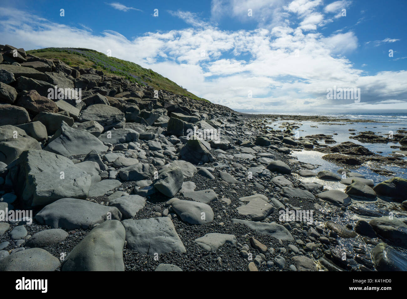 Iceland - Green hill behind stony shore and reflecting water of blonduos coastline Stock Photo