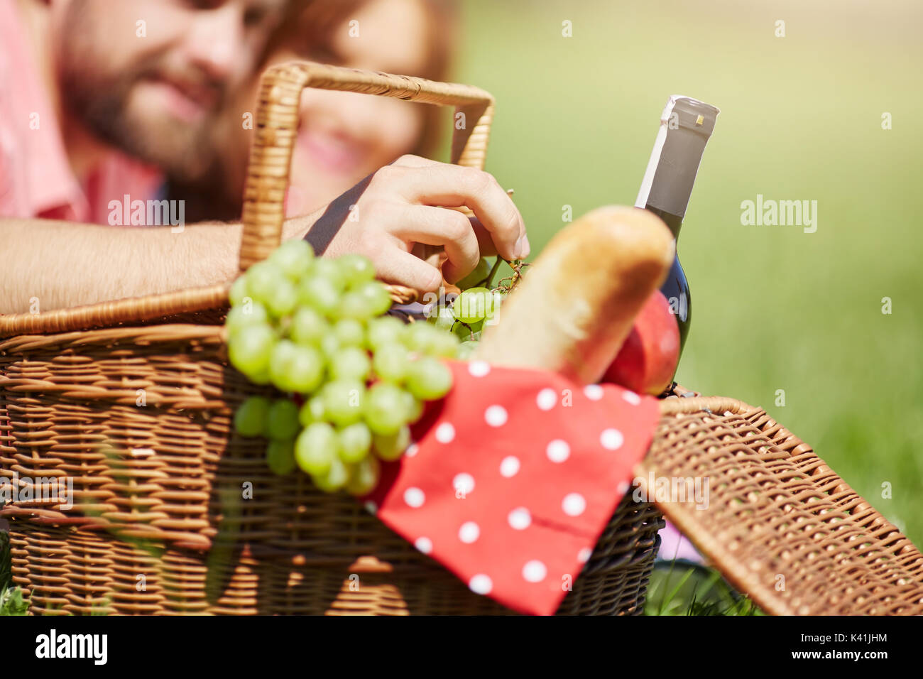 A photo of picnic basket full of food and drink. A man is reaching for