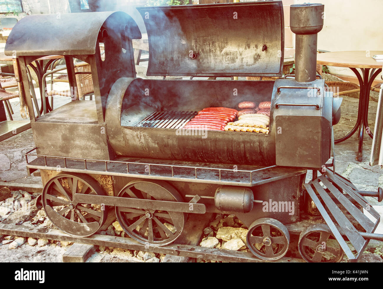 Barbecue grill with meat in shape of old steam locomotive. Bbq scene.  Garden reastaurant. Yellow photo filter Stock Photo - Alamy