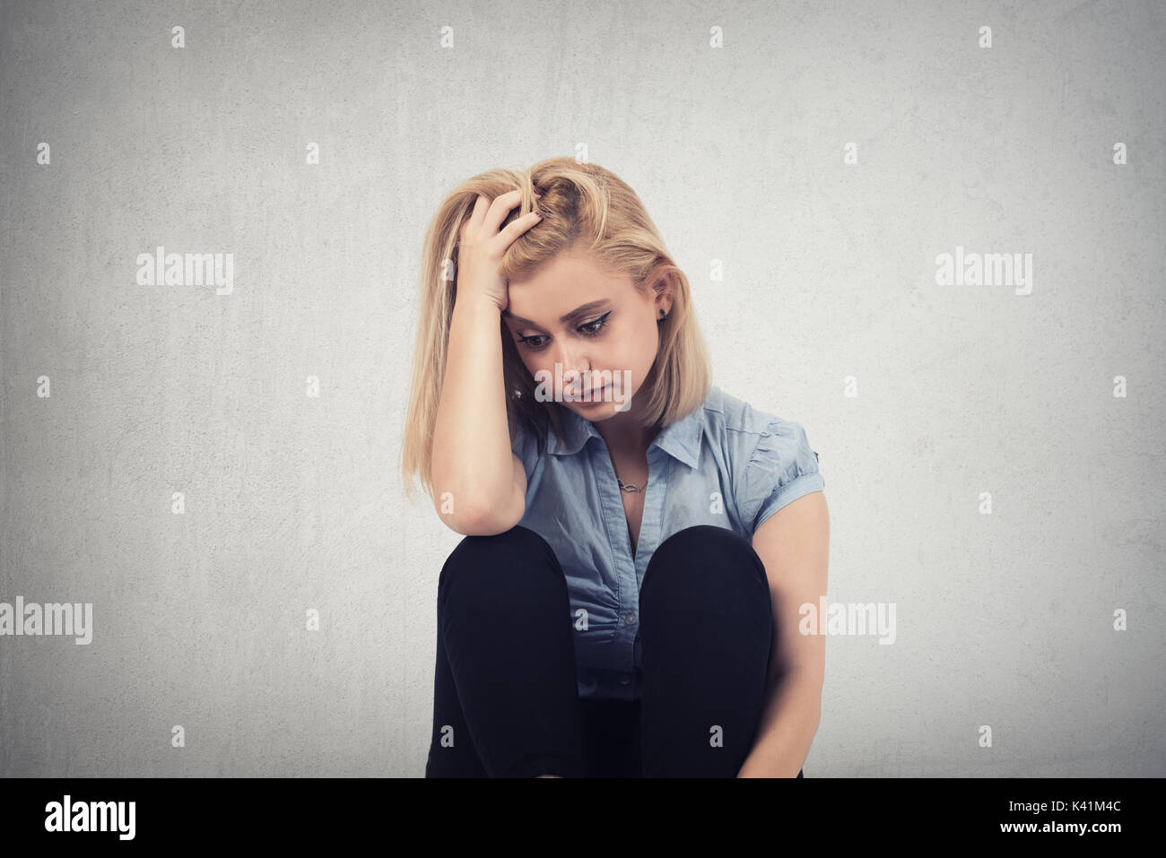 one sad woman sitting on the floor near a wall and holding her head in her hands Stock Photo