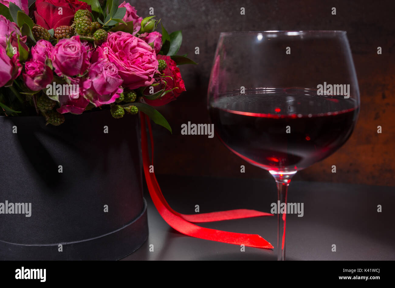 Close up of glass with wine standing by bouquet of pink roses Stock Photo