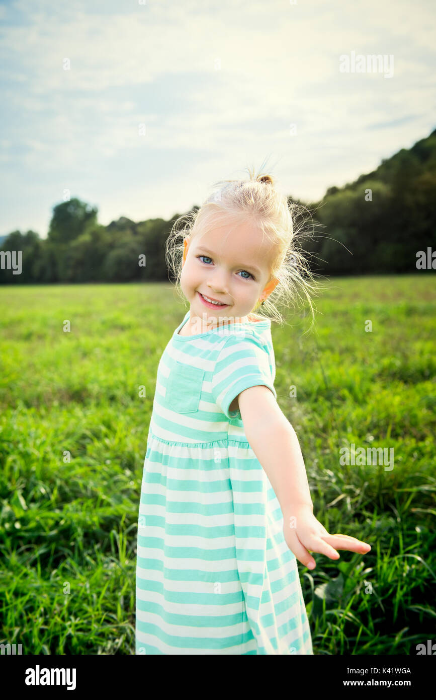Adorable blond little girl with cheeky smile, outdoors play time Stock Photo