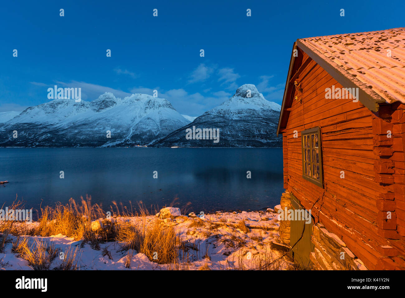 Wooden cabin of fisherman illuminated surrounded by the frozen sea at dusk Storfjorden Lapland Lyngen Alps Tromsø Norway Europe Stock Photo