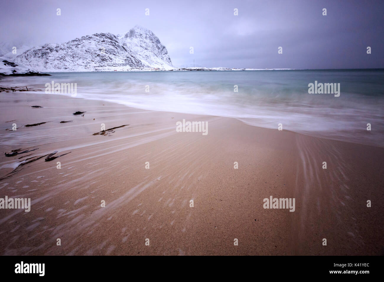 Waves of the icy sea on the beach in the background the snowy peaks Pollen Vareid Flakstad Lofoten Islands Norway Europe Stock Photo