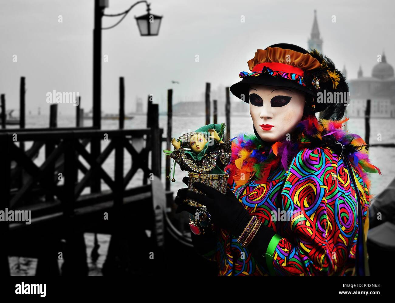 A person in a costume full of bright colours holding a small doll at the Carnival of Venice Stock Photo