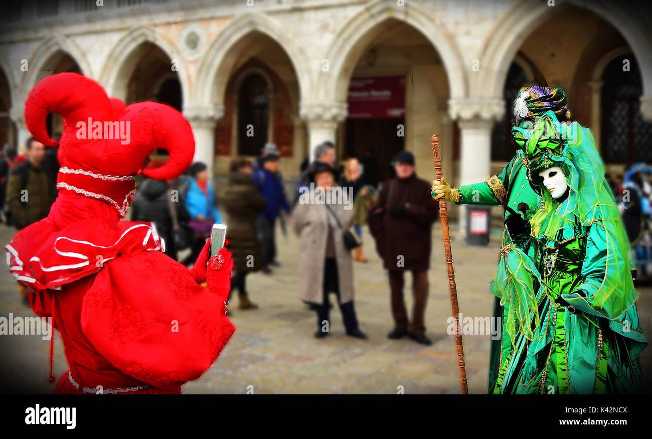 A person in red joker costume at the carnival of Venice takes a photo of two other costumed masquerades with his mobile phone. Stock Photo