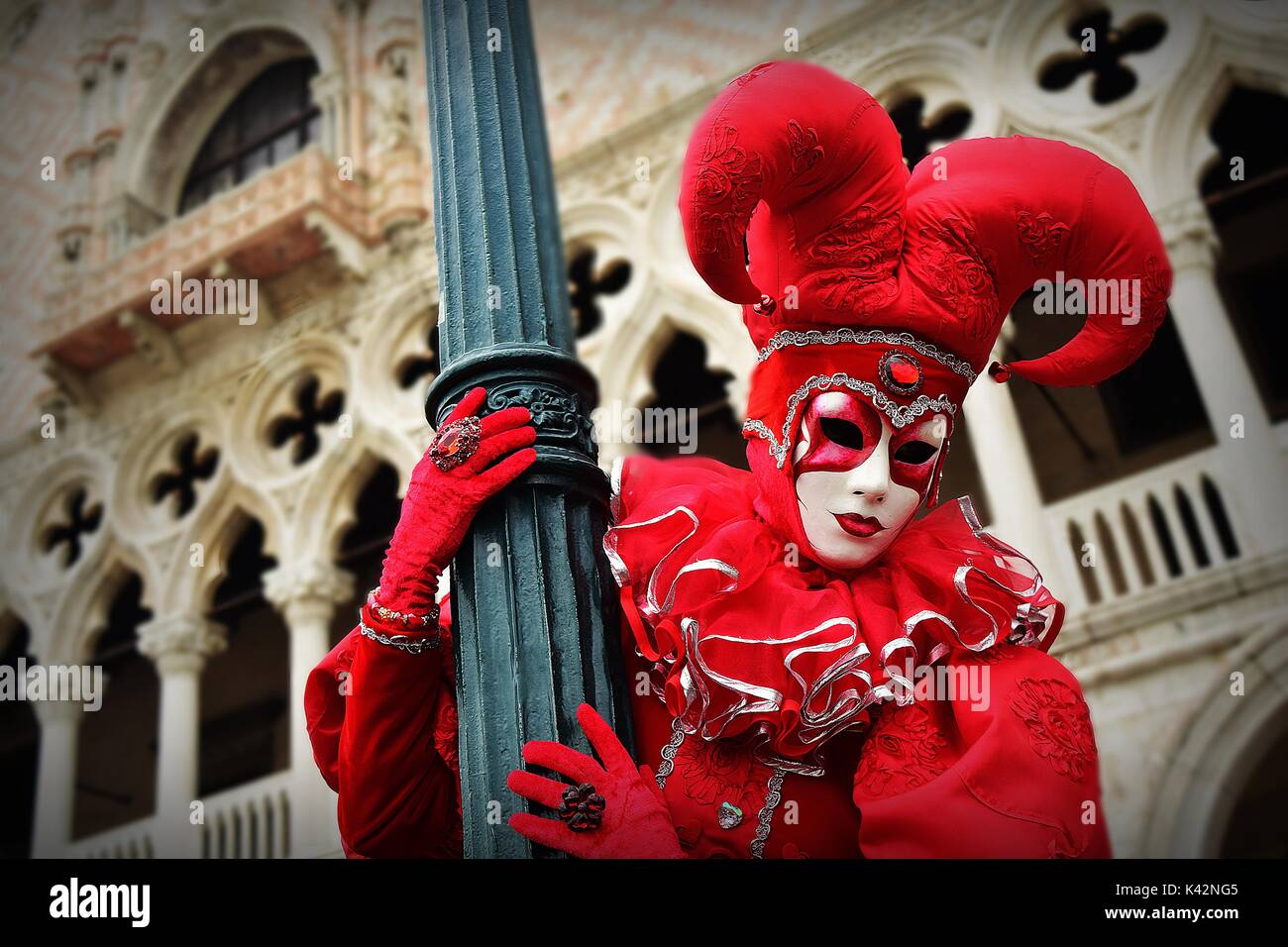 A person in a red joker costume hanging on to a lamp post during a masquerade at the Carnival of Venice. Stock Photo