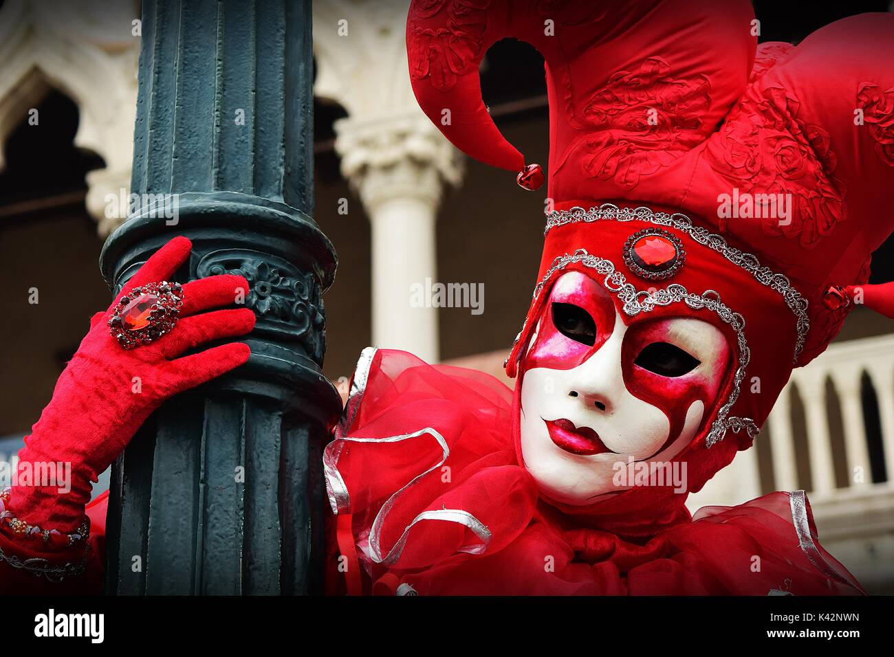 A person in a red joker costume hanging on to a lamp post during a masquerade at the Carnival of Venice. Stock Photo
