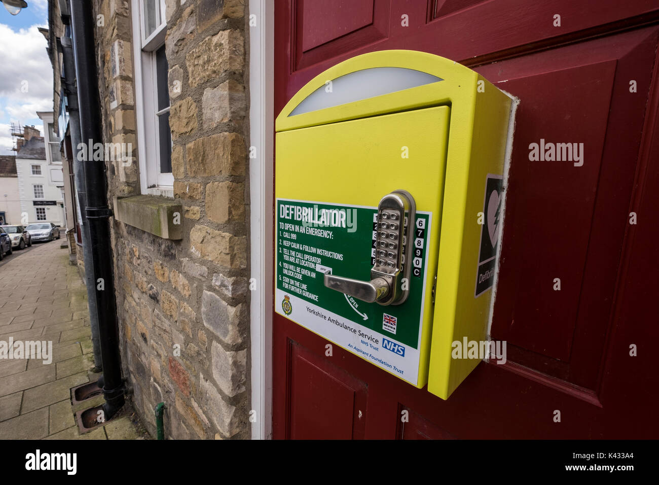 Public defibrillator in a yellow box fixed to a door in Richmond town center, North Yorkshire Dales, England, UK Stock Photo