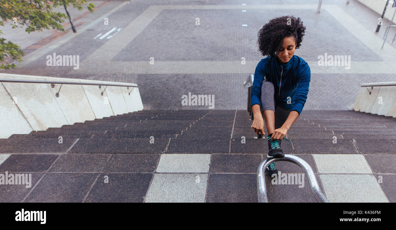 Woman runner tying her shoe lace on the railing of stairs. Curly haired ...