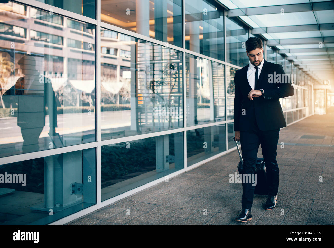 Businessman carrying a suitcase and looking at his watch while walking in airport. Business traveler checking time on his wristwatch. Stock Photo