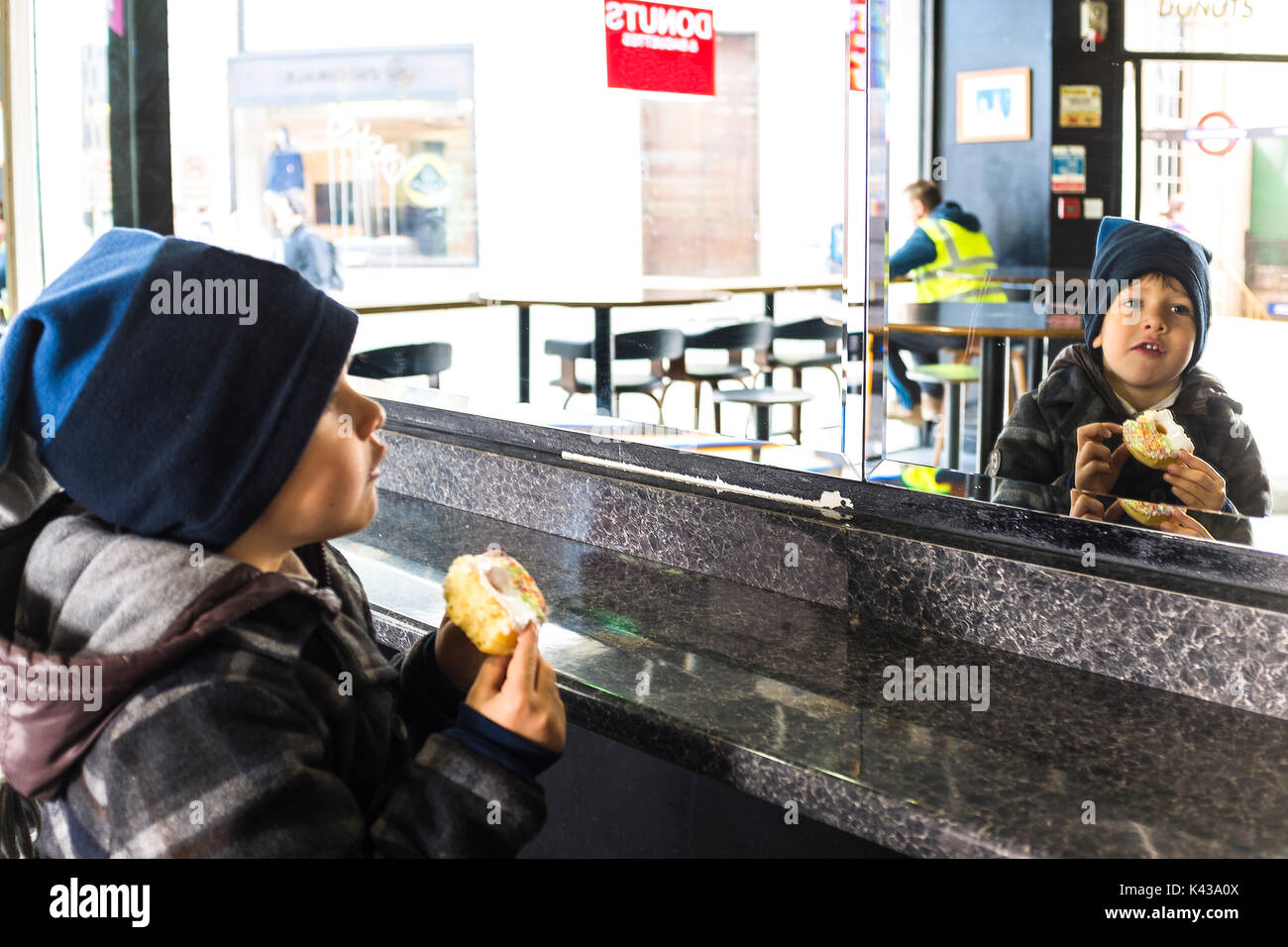 Boy eating sweet donut and looking at the mirror Stock Photo - Alamy