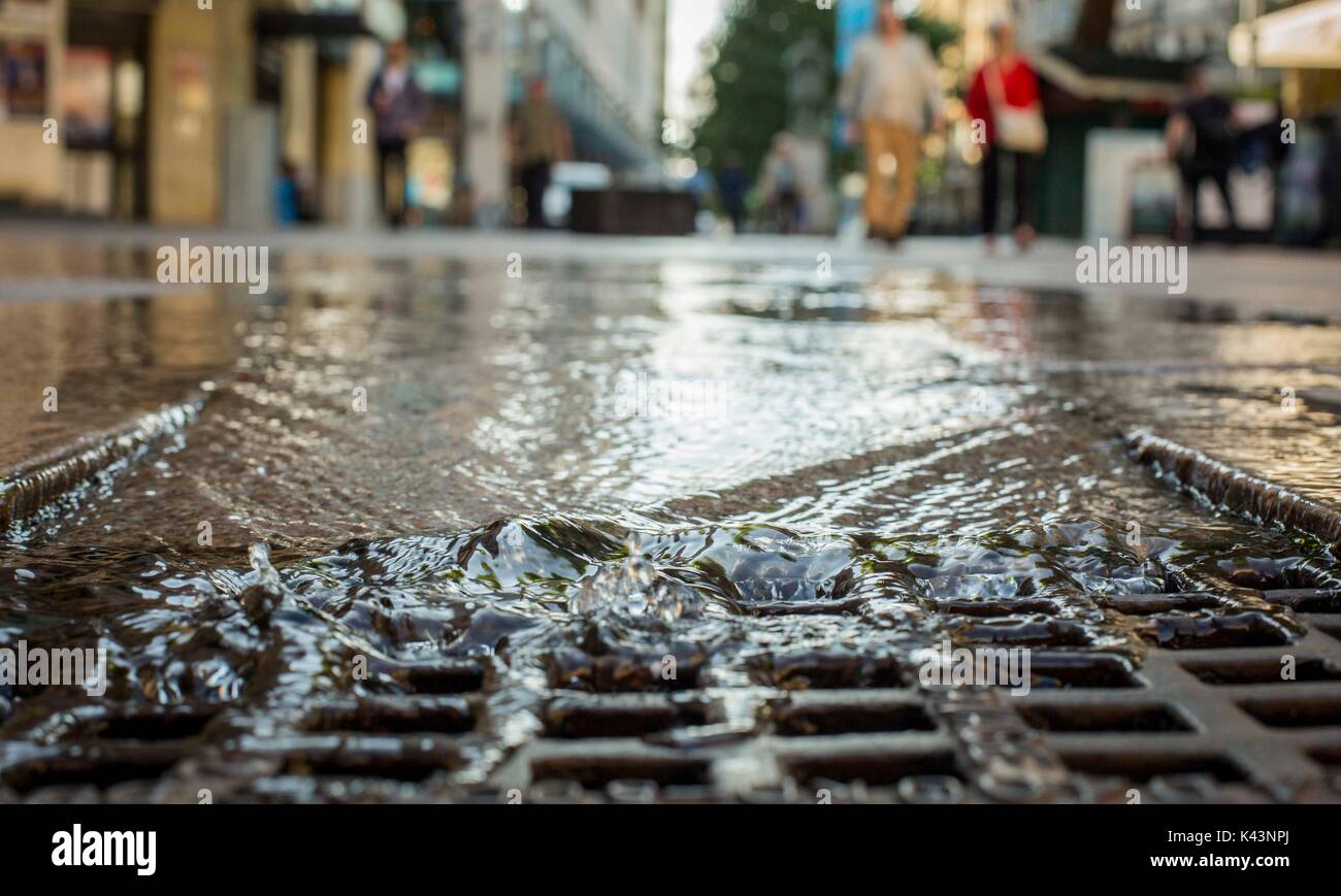 A stream of water from a burst pipe running into a city centre drain
