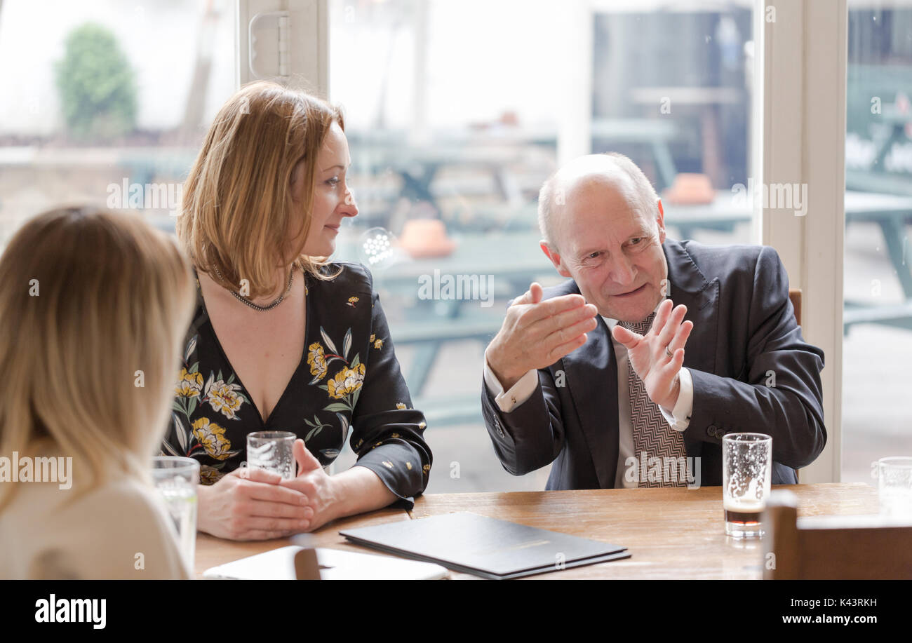 Professional real people, young adult woman, senior man, having informal business meeting in pub at glass of dark beer. Candid unposed horizontal shot Stock Photo