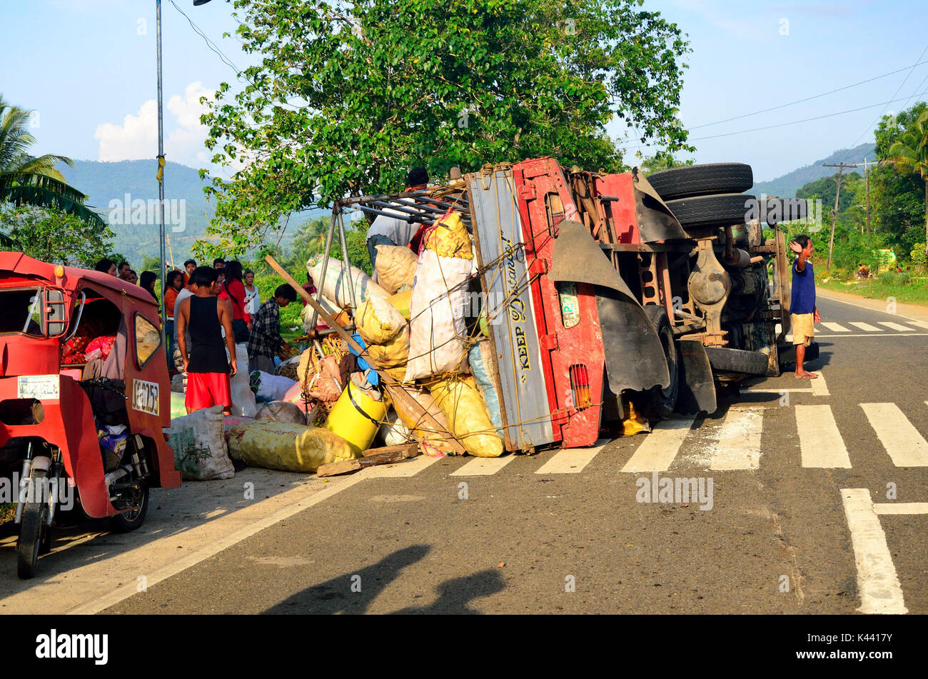 SISON, PHILIPPINES - 16 OCT 2012 Overturned truck on road in Mindinao with bystanders. Road accident leaves vehicle lying on side, with load spilled Stock Photo